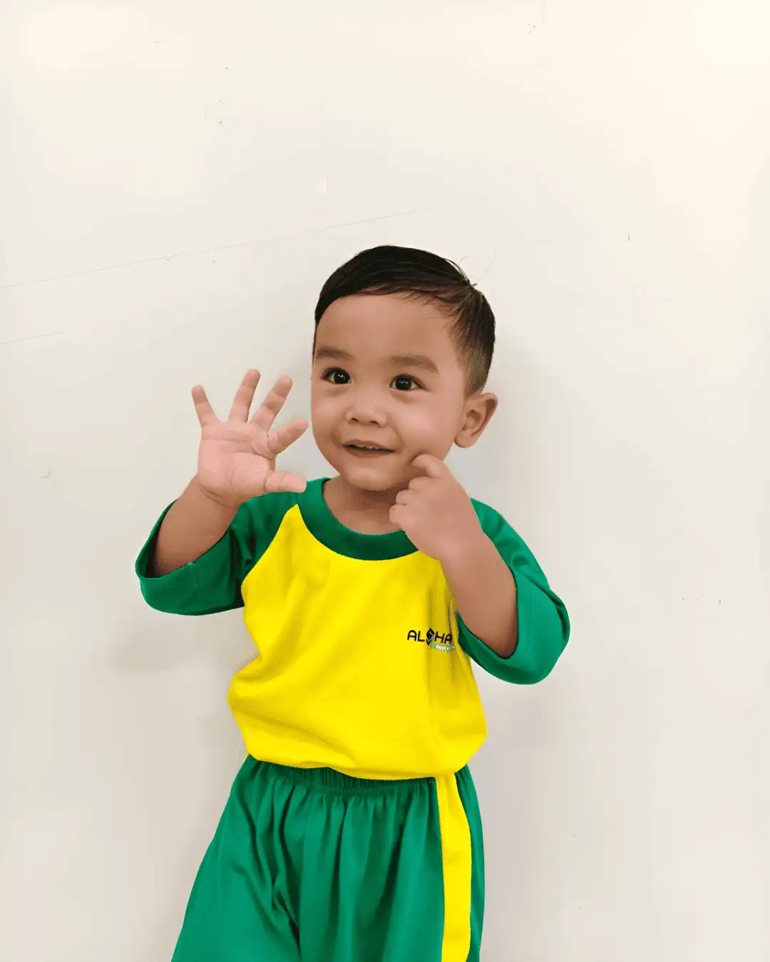 A child smiling and waving, wearing a green and yellow outfit